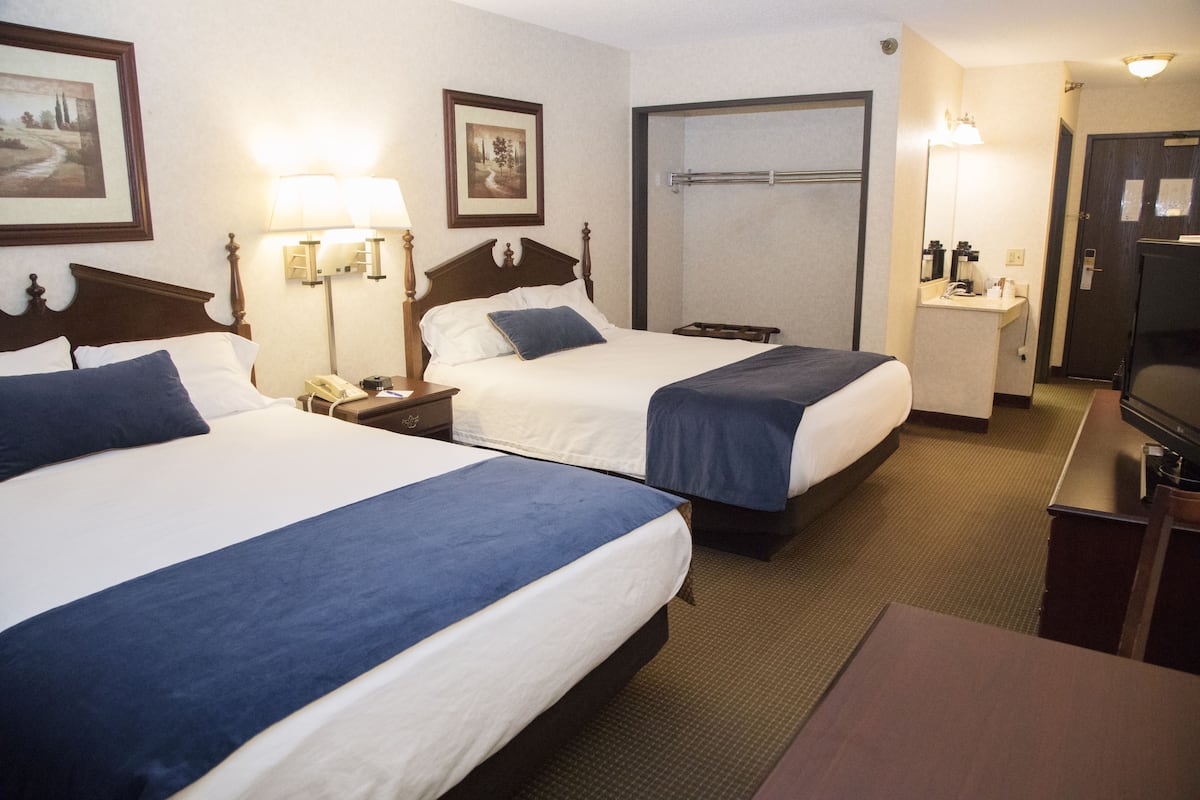 Ein Hotelzimmer mit zwei Betten, einem Schreibtisch, einem Fernseher und einem durch eine offene Tür einsehbaren Badezimmer.