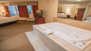 Una camera d'albergo con una vasca da bagno ampia, un letto, una televisione e una finestra con tende.
