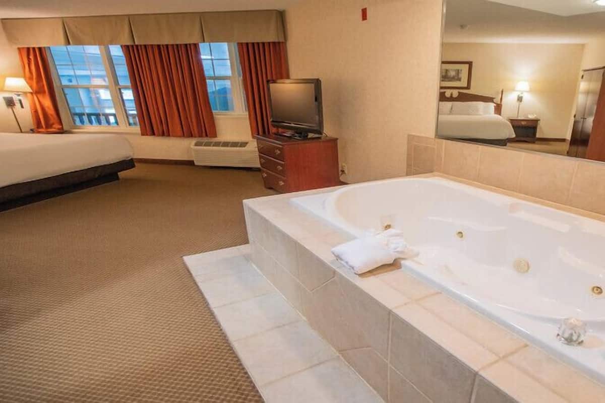 Ein Hotelzimmer mit einer großen Badewanne, einem Bett, einem Fernseher und einem Fenster mit Vorhängen.