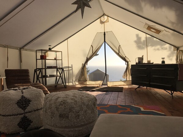 A tent with a view of the ocean, a chair, a shelf, and a dresser. - Terra Glamping (Stewarts Point)