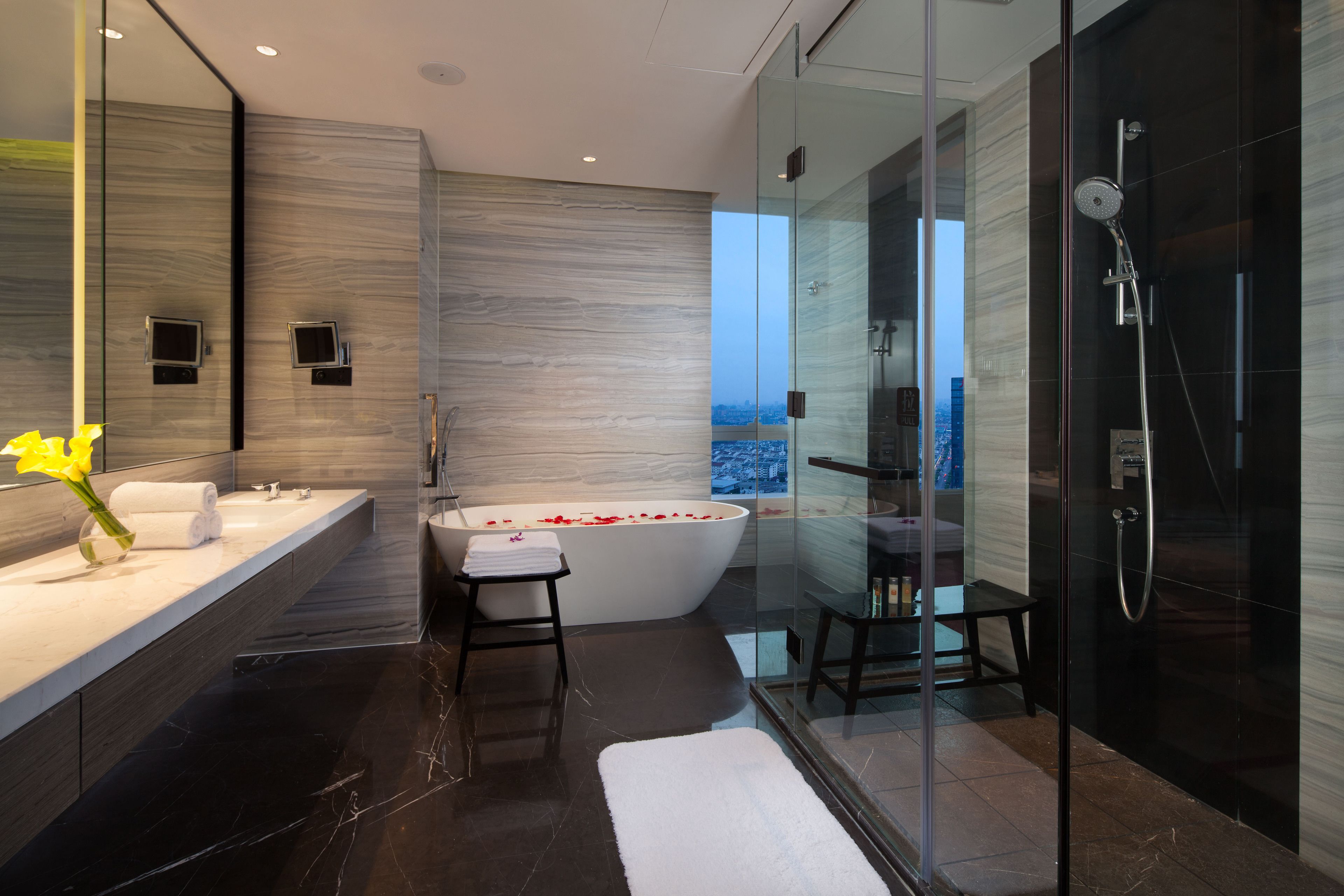 Une salle de bain moderne dotée d’une grande baignoire, d’une douche à parois de verre et offrant une vue sur la ville.