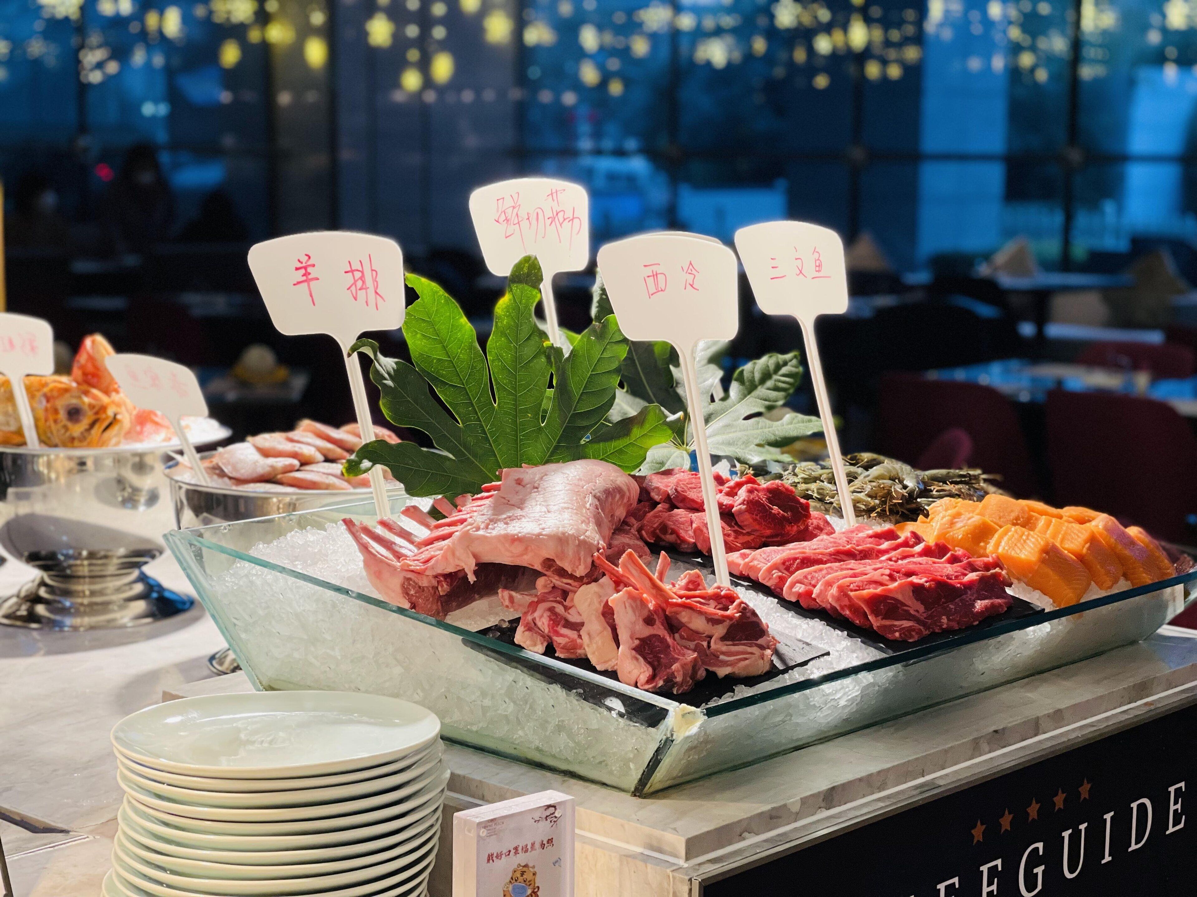 Ein Buffet mit verschiedenen Fleisch- und Fischspeisen, inklusive Schildern in einer Fremdsprache.