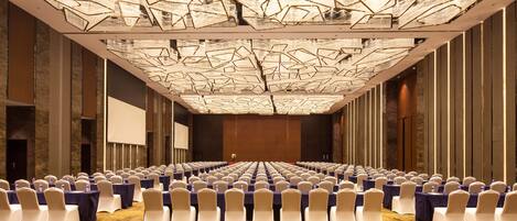 Ein Konferenzraum mit Tischen und Stühlen, einer großen Leinwand und einer gemusterten Decke.
