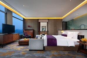 A modern hotel room with a large bed, a flat-screen TV, a seating area with a sofa and armchair, and a view of the cityscape through large windows. - Crowne Plaza Kunshan by IHG (Suzhou)