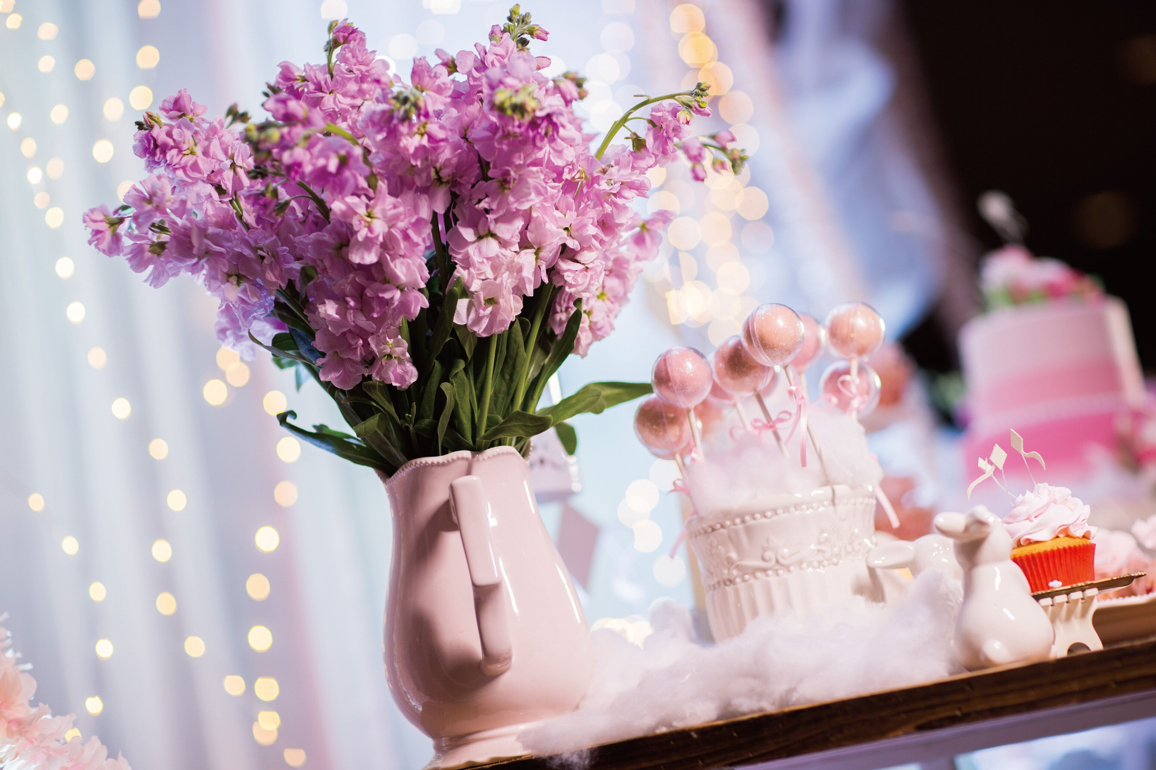 Una mesa con un jarrón de flores moradas, un pastel y varios objetos decorativos.