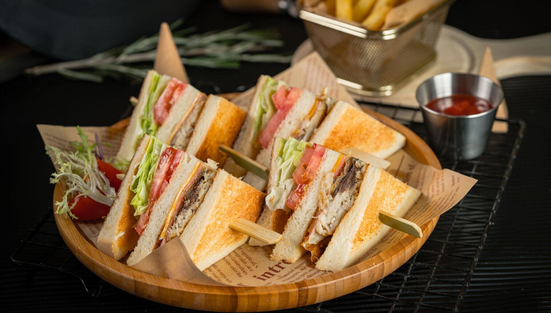 Un plateau en bois avec des sandwichs grillés, un panier de frites et un petit pot de ketchup.
