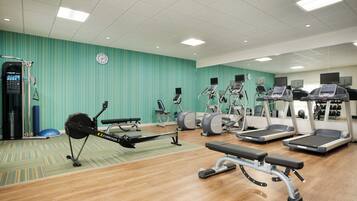 Une salle de sport équipée de divers appareils d’exercice, notamment des tapis de course, des vélos elliptiques et un rameur.