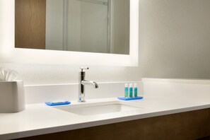 A bathroom with a white sink, a mirror above it, and a wooden vanity. - Holiday Inn Express & Suites McAllen - Medical Center Area by IHG (McAllen)