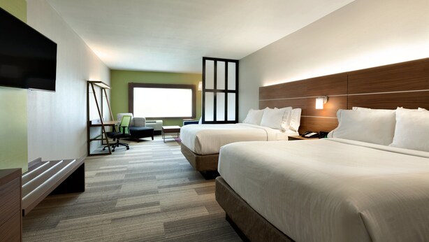 Ein Hotelzimmer mit zwei Betten, einem Schreibtisch mit Stuhl, einem Fernseher und einem großen Fenster.