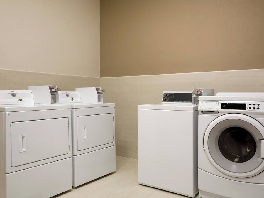 A laundry facility with stacked washers and dryers, control panels, and a tiled floor.