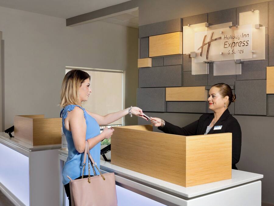 A reception desk with a sign indicating 'Holiday Inn Express & Suites' and a woman handing over a card to a receptionist.