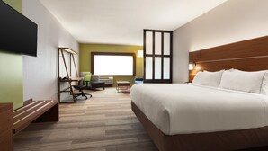 Ein Hotelzimmer mit einem großen Bett, einem Schreibtisch mit Stuhl, einem Fernseher und einem Fenster mit Jalousien.