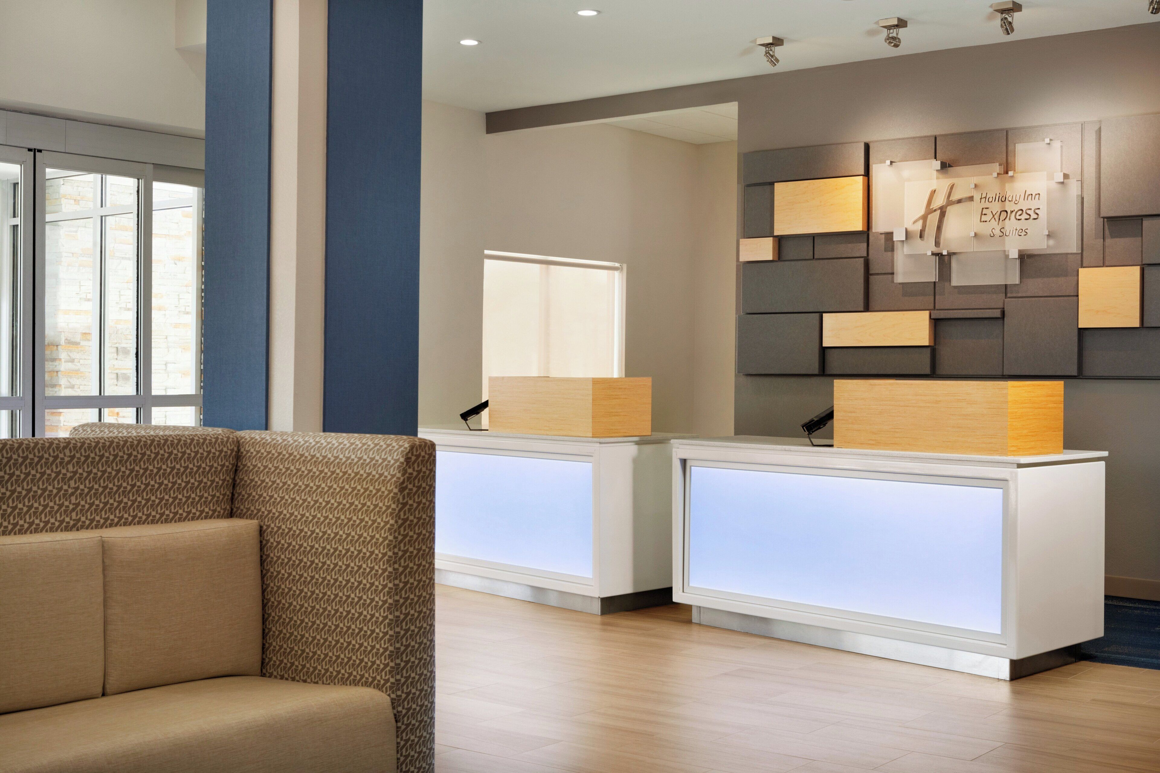 A reception area with a modern design, featuring a reception desk, a seating area with a patterned sofa, and a wall with a geometric design and a sign.