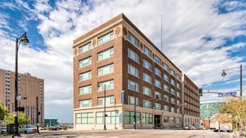 A multi-story building with a brick facade, large windows, and a street view with traffic lights and vehicles.