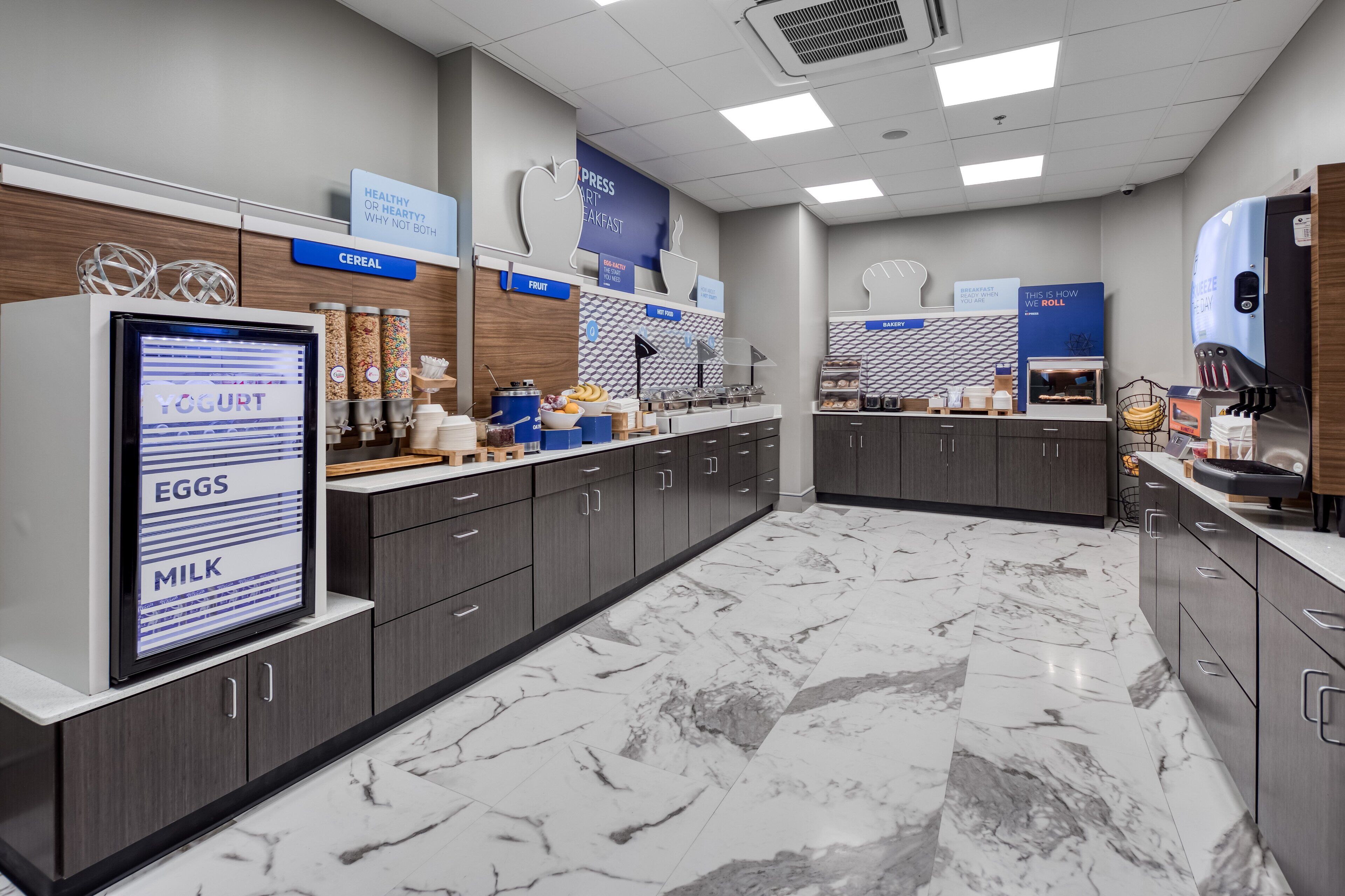 A modern breakfast area with a digital menu display, marble flooring, and neatly organized food stations.