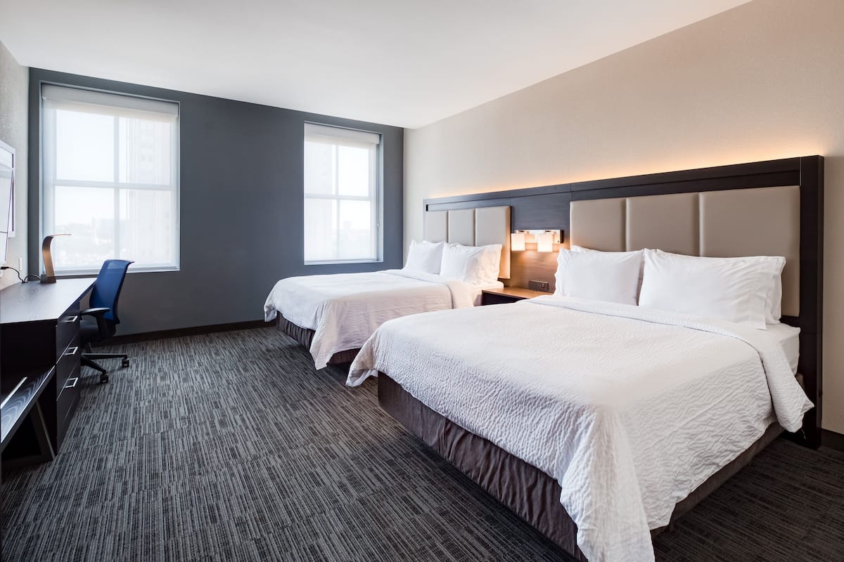 A hotel room with two beds, a desk, and a chair.