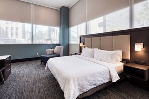 A hotel room with a large bed, a desk, a chair, and a view of the city through large windows. - Holiday Inn Express Kansas City Downtown by IHG (Kansas City)