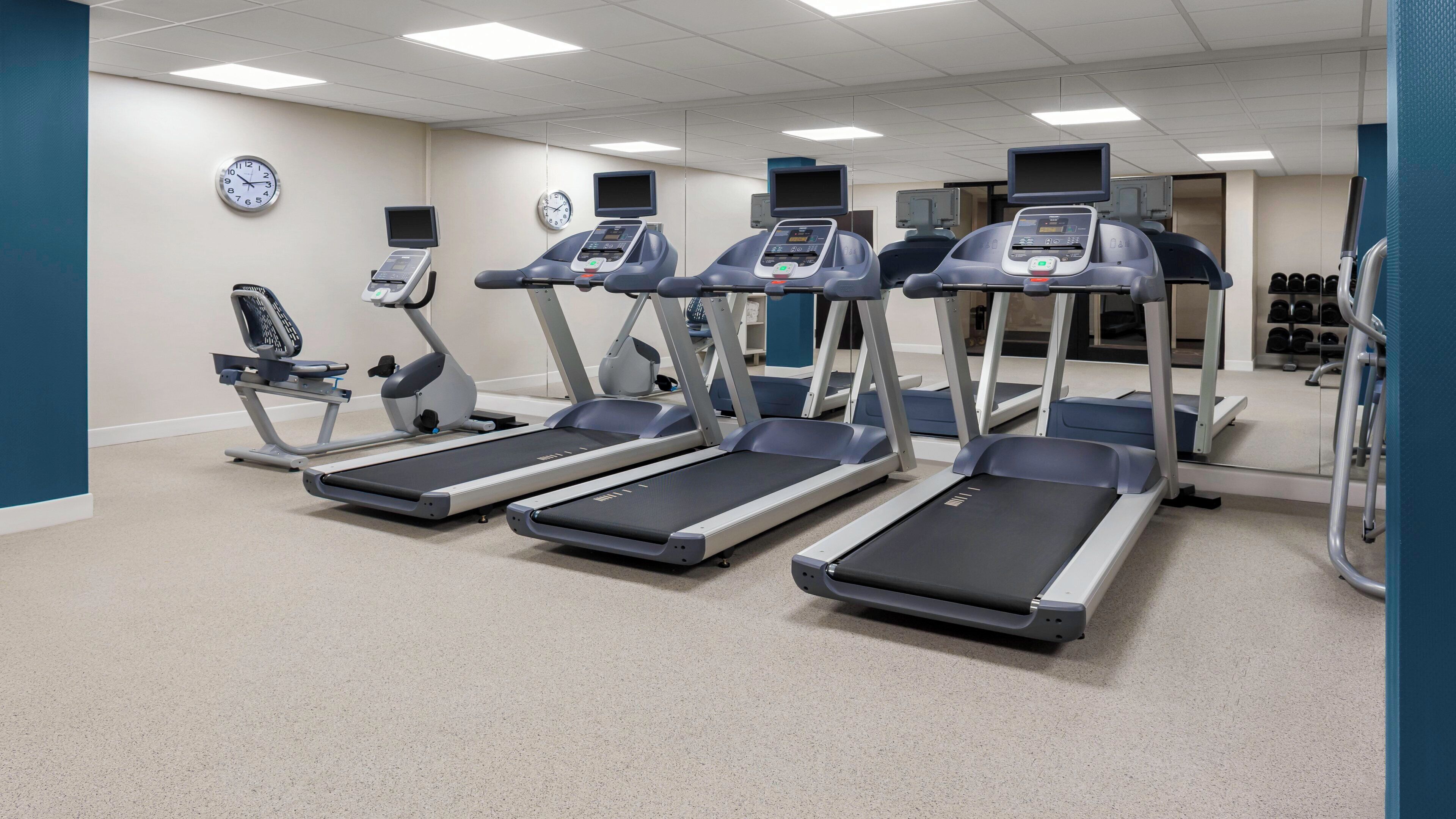 A fitness center with treadmills, elliptical machines, and a wall clock.