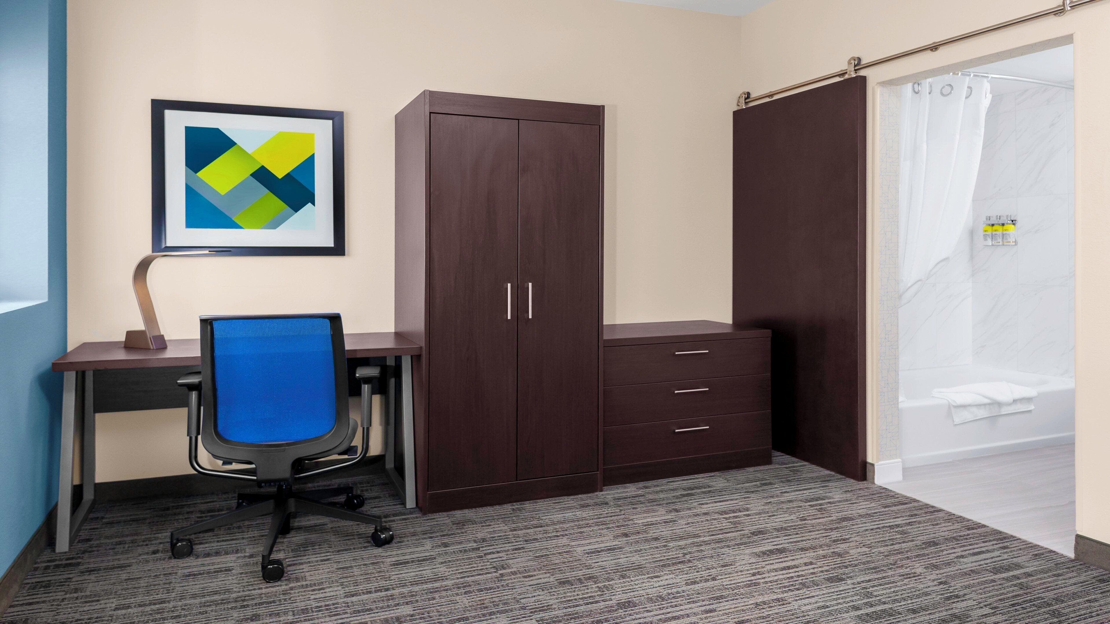A hotel room with a desk, chair, wardrobe, and a shower area.