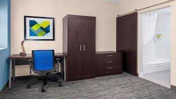 A hotel room with a desk, chair, wardrobe, and a shower area.