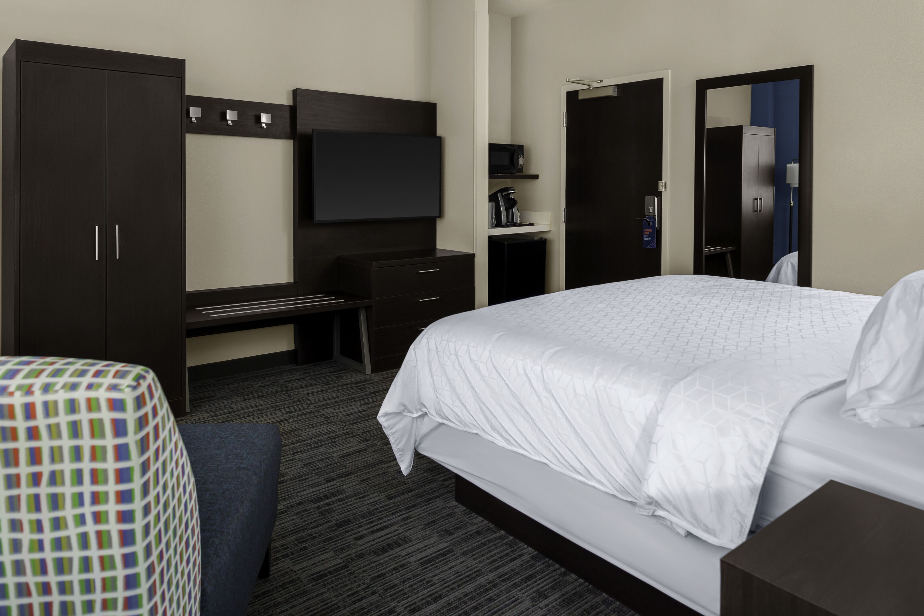 Una habitación de hotel con cama, escritorio, armario, televisor y microondas.