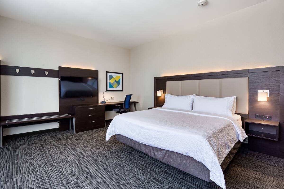 A hotel room with a large bed, a desk with a chair, a flat-screen TV, and a painting on the wall.