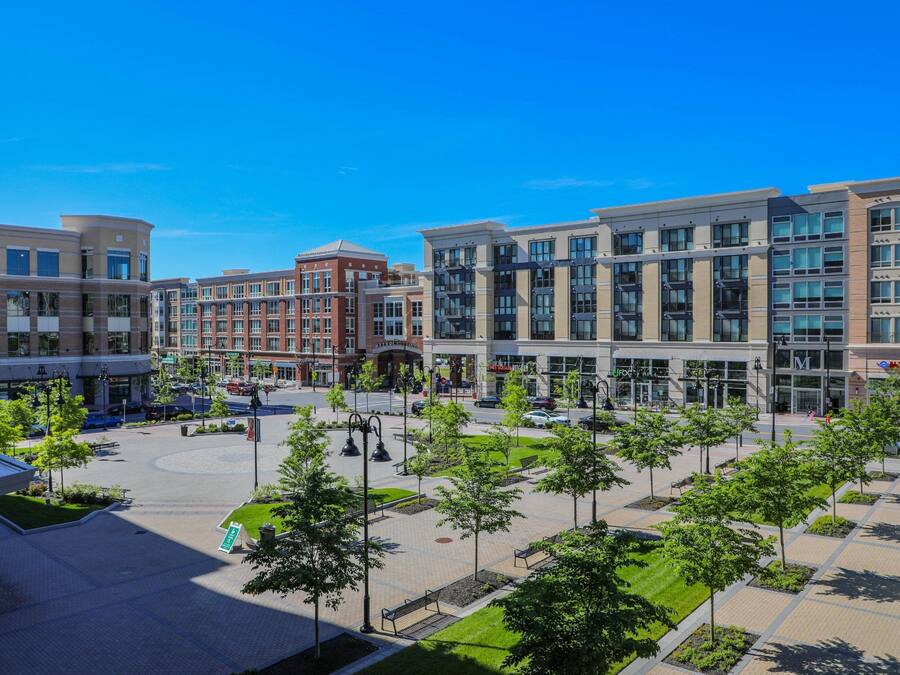A modern urban plaza with a central roundabout, surrounded by multi-story buildings with commercial establishments.
