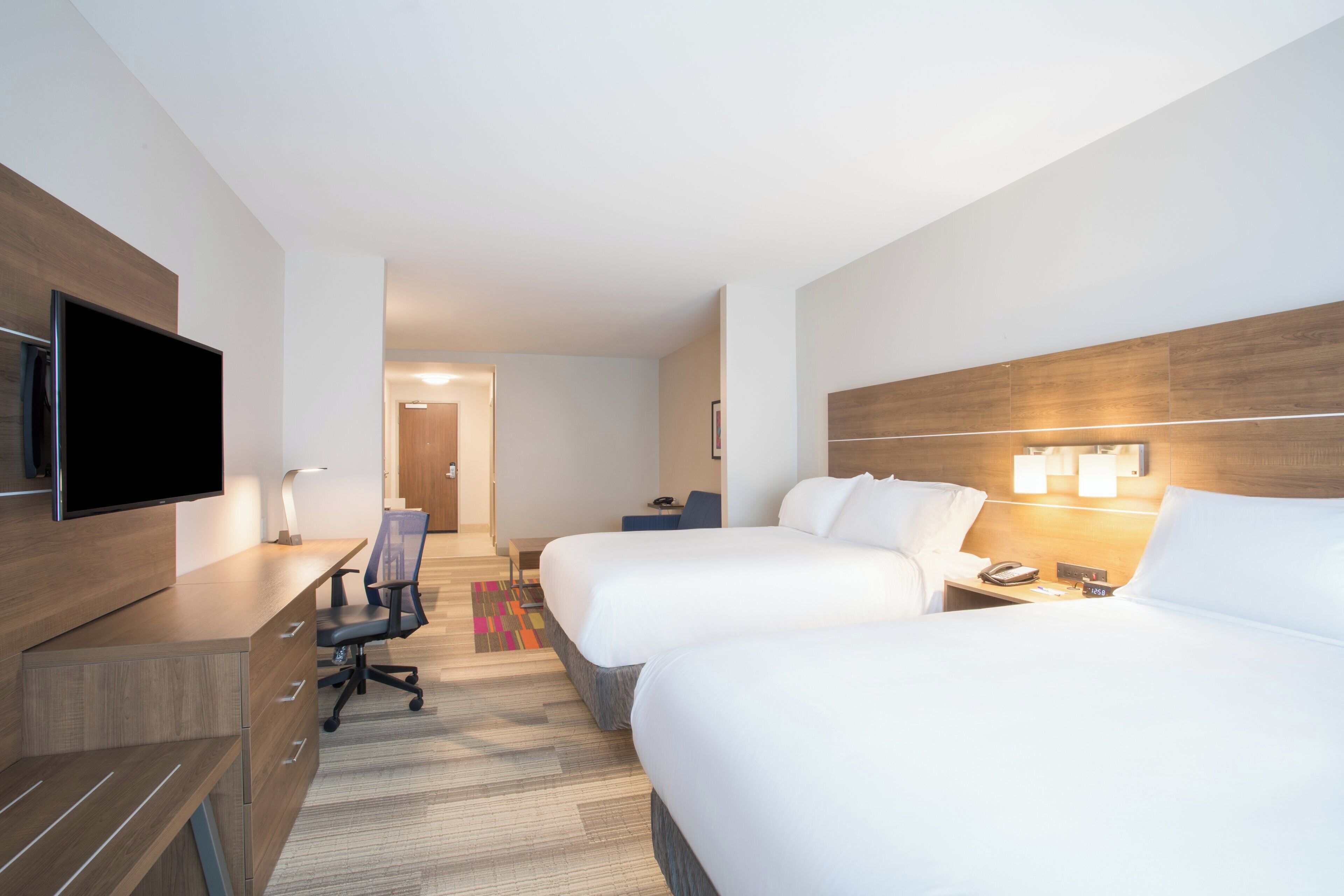 Una camera d'albergo con un letto, una scrivania, una sedia, una TV e lampade da comodino.