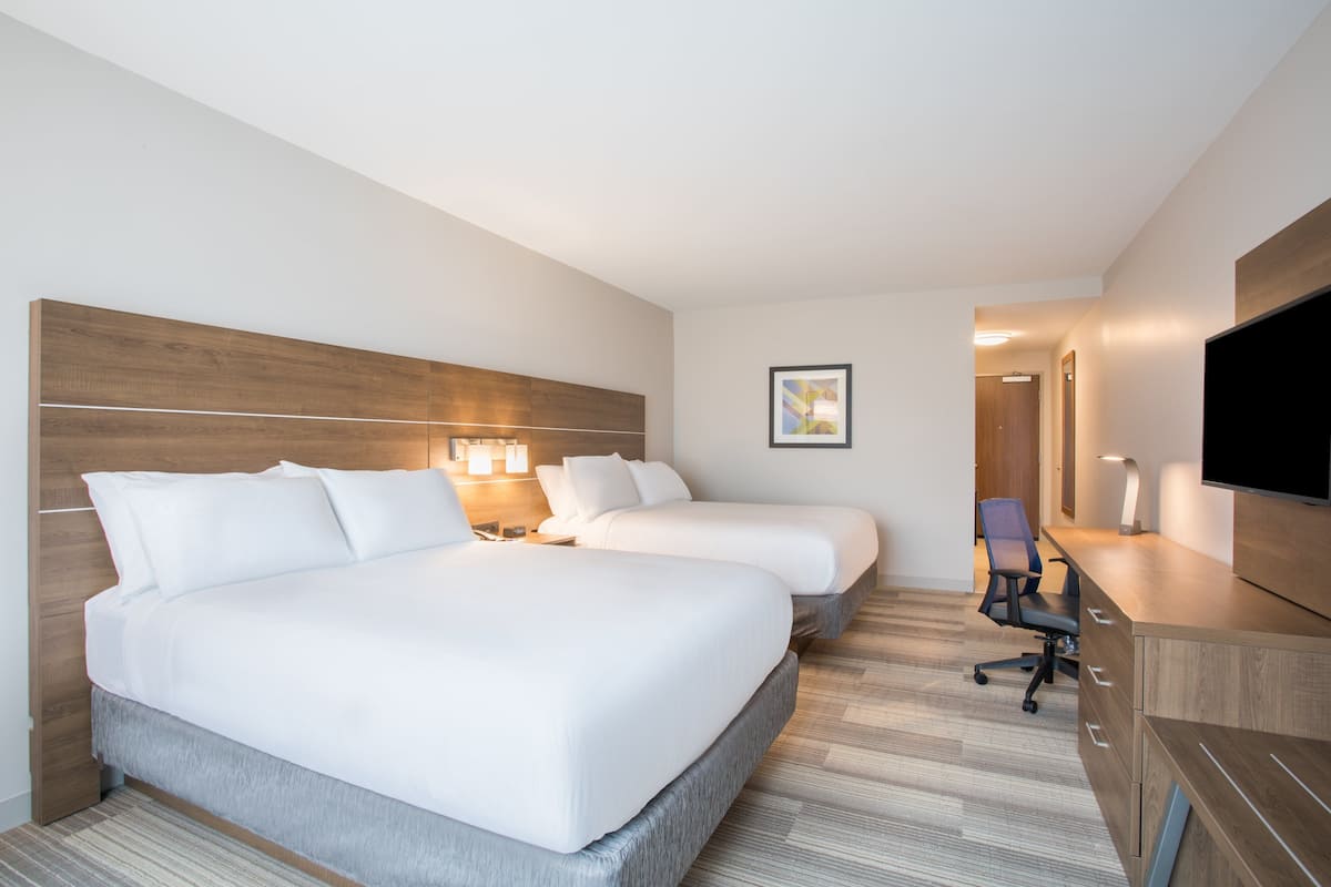 A hotel room with two beds, a desk, a chair, a TV, and a framed picture on the wall.