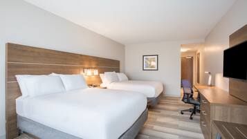 A hotel room with two beds, a desk, a chair, a TV, and a framed picture on the wall.