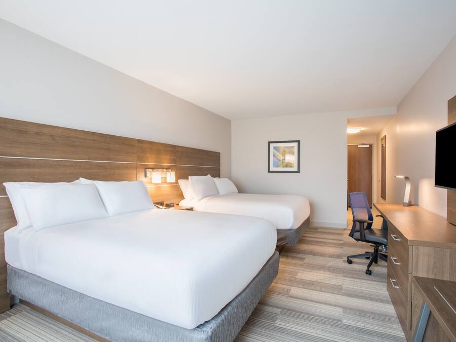 A hotel room with two beds, a desk, a chair, a TV, and a framed picture on the wall.