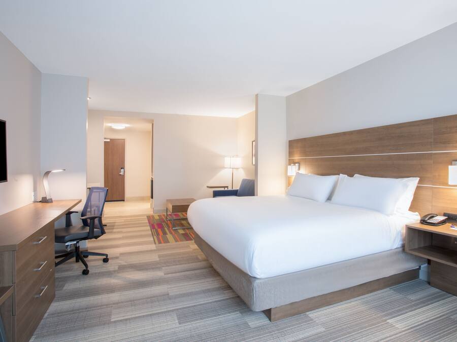 A hotel room with a large bed, a desk with a chair, a TV, and a nightstand with a lamp.