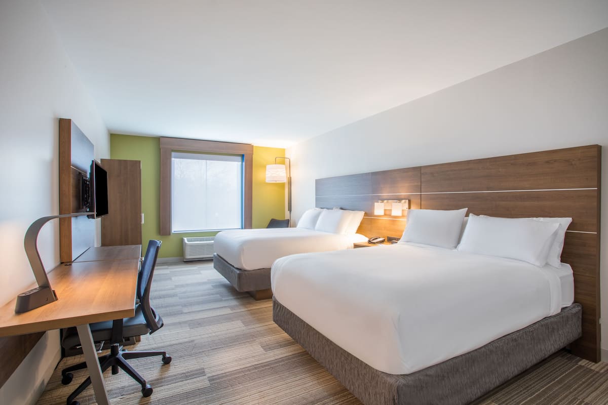 A hotel room with two beds, a desk, a chair, a TV, and a window.