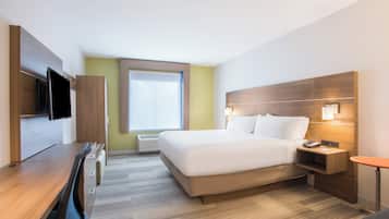Una habitación de hotel con cama, escritorio, televisión, mesita de noche con lámpara y ventana.
