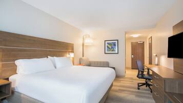 A hotel room with a large bed, a desk, a chair, a television, and a door leading to another room.