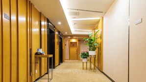 Un couloir d’hôtel avec des lambris en bois, un comptoir de réception, une plante et un tapis à motifs rayés.