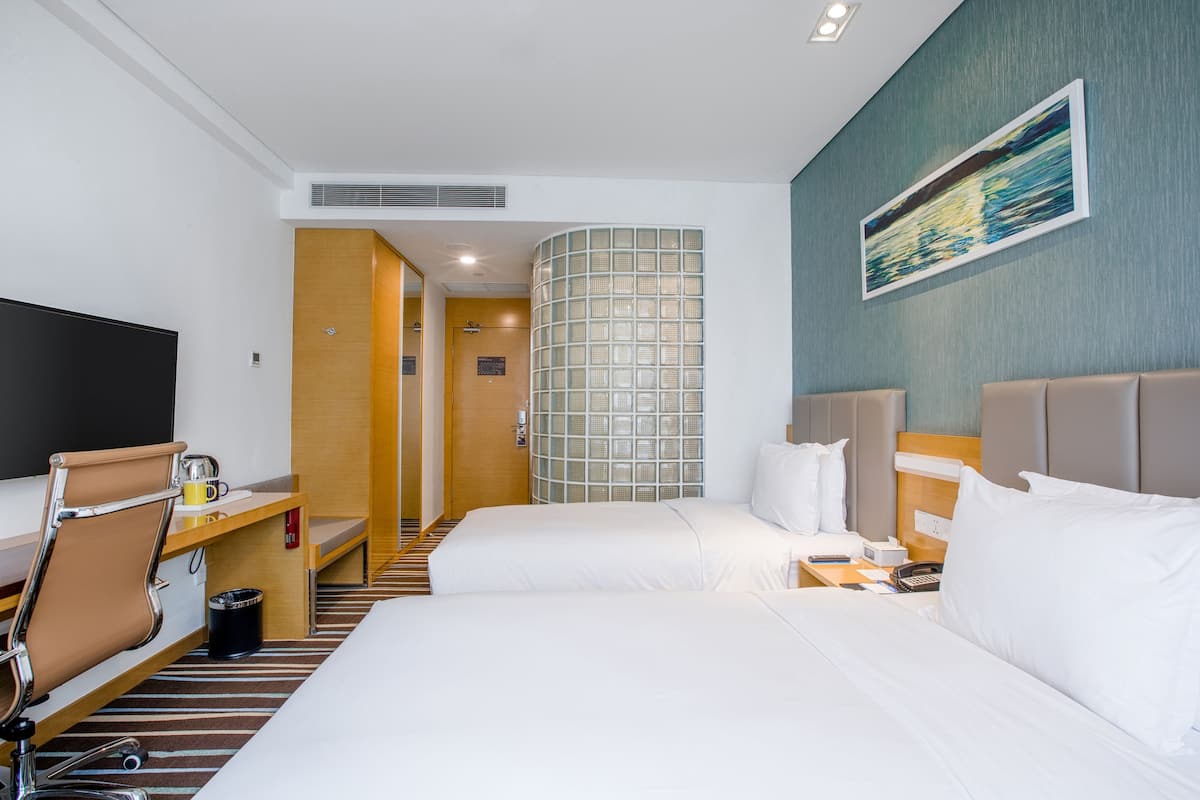 Una camera d'albergo con un letto, una scrivania, una sedia, una televisione e l'ingresso del bagno.