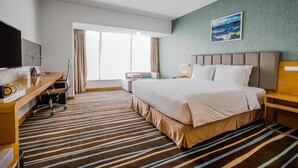 Une chambre d’hôtel avec un grand lit, un bureau avec une chaise, une télévision et une fenêtre avec des rideaux.