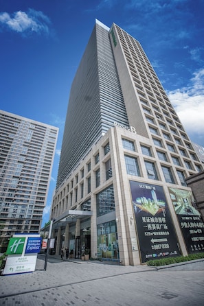 Ein modernes Hochhaus mit einem auffälligen 'BlockB'-Schild, umgeben von anderen Gebäuden, und einem klaren Himmel.