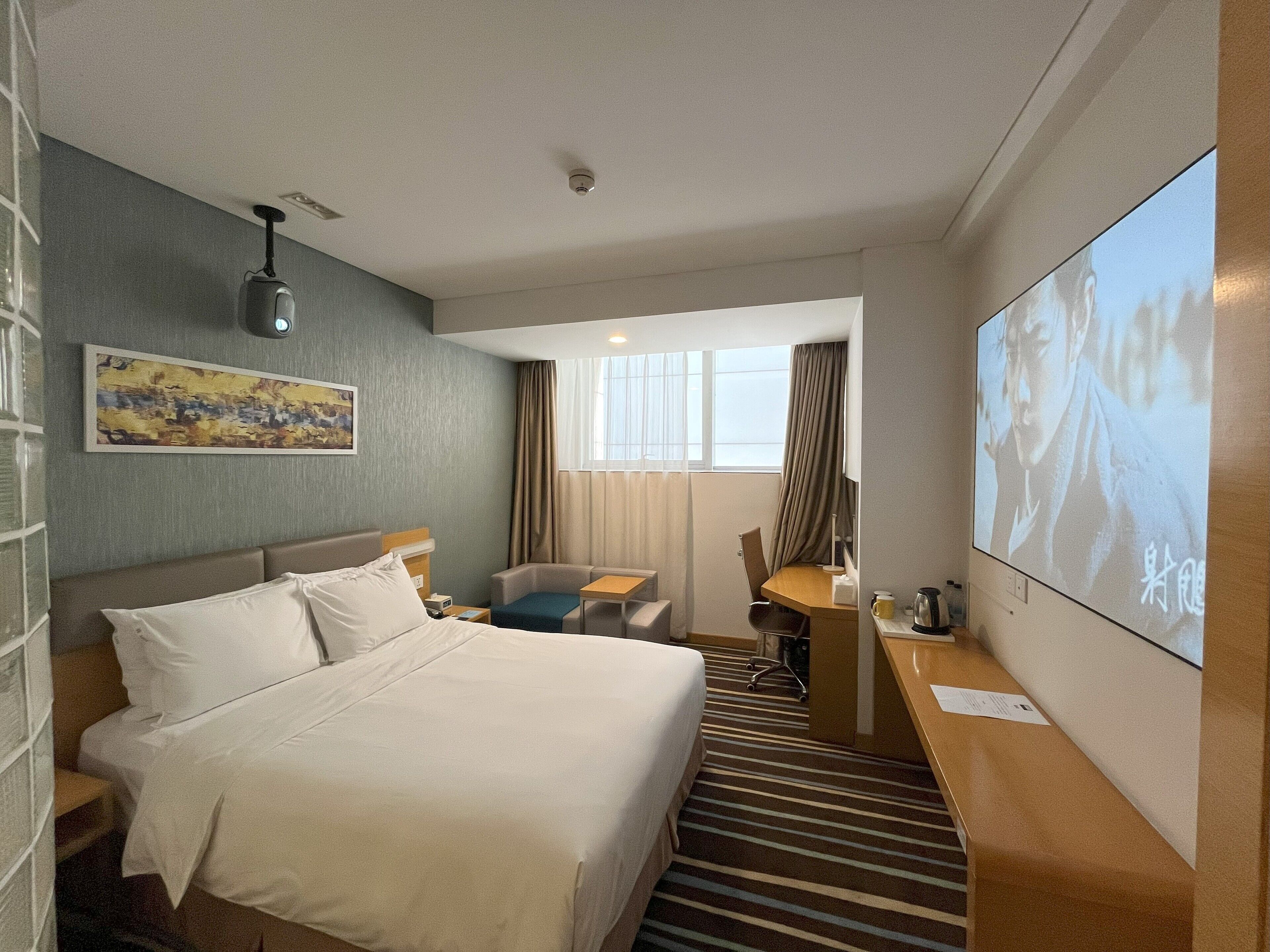 Un cuarto de hotel con cama, escritorio, silla, televisor y un cuadro en la pared.