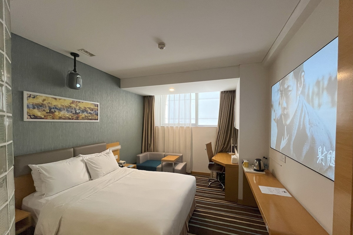 Una camera d'albergo con un letto, una scrivania, una sedia, una televisione e un quadro appeso al muro.