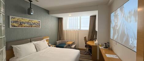 A hotel room with a bed, a desk, a chair, a television, and a painting on the wall.