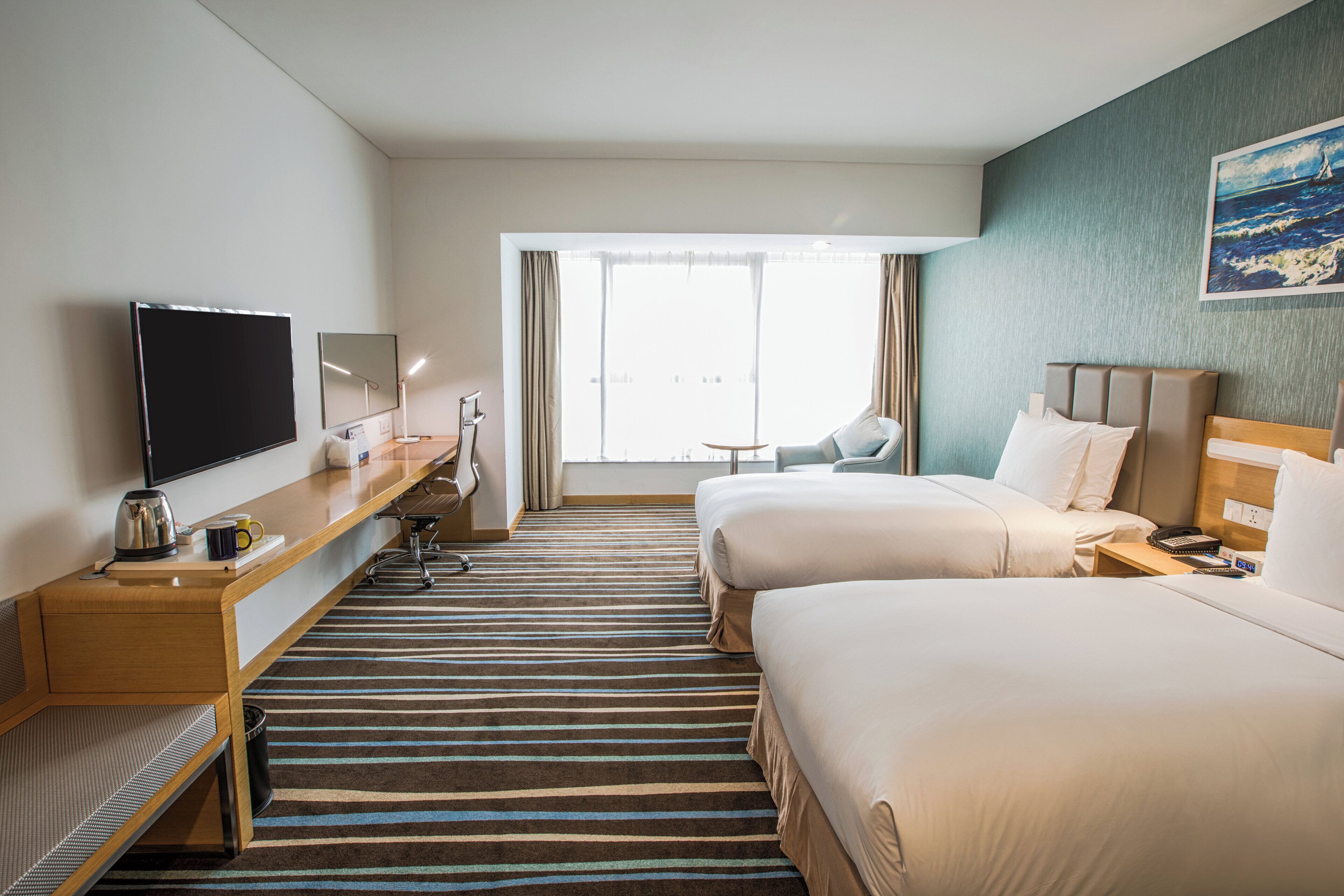 Habitación de hotel con dos camas, un escritorio con televisor, una silla y una ventana con cortinas.