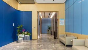 Un hall d’entrée moderne avec un mur bleu incurvé, un comptoir d’accueil, un espace salon et un couloir menant aux ascenseurs.