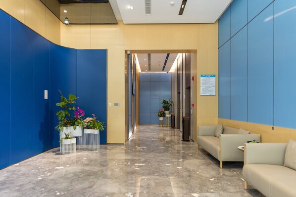 A modern lobby with a curved blue wall, a reception desk, a seating area, and a hallway leading to elevators.