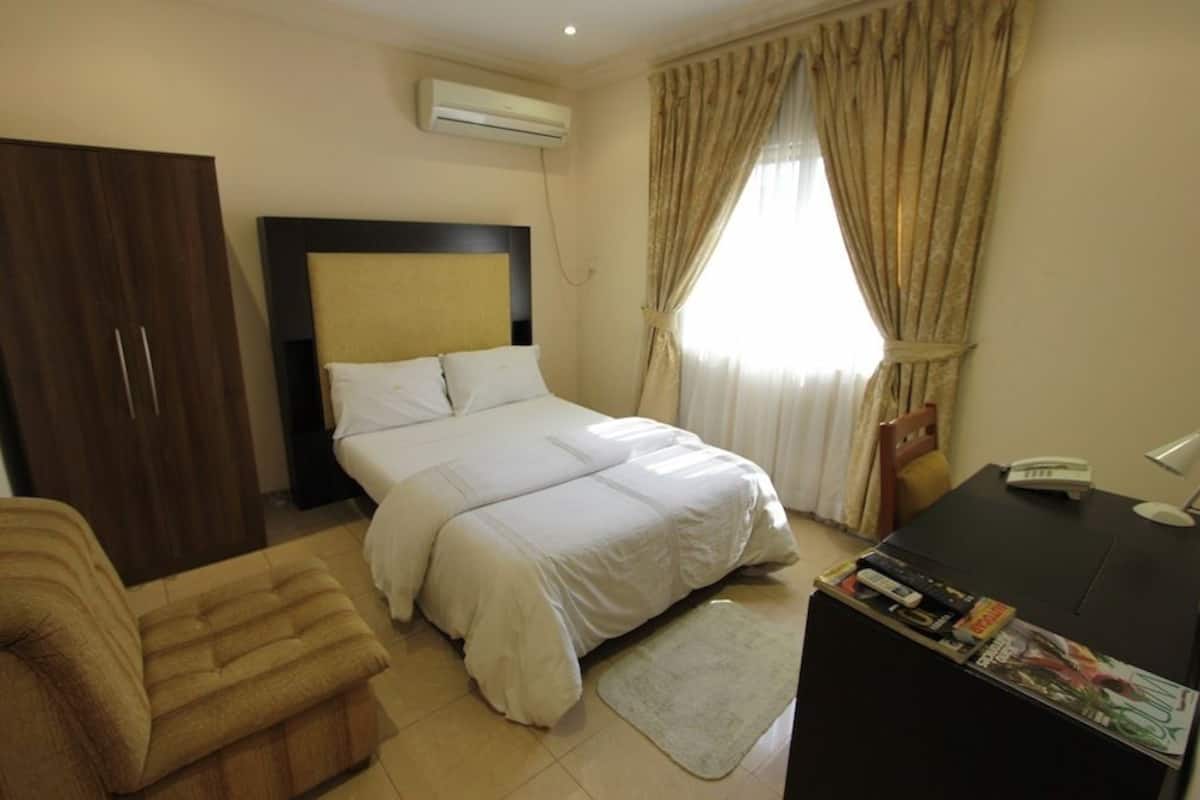 Ein Hotelzimmer mit Bett, Schreibtisch, Stuhl, Kleiderschrank und einem Fenster mit Vorhängen.