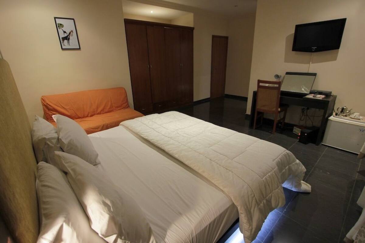 Ein Hotelzimmer mit einem Bett, einem Schreibtisch, einem Stuhl, einem Kleiderschrank und einem Fernseher.