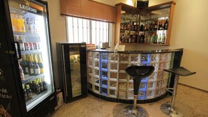 A bar area with a refrigerator stocked with beverages, a counter with a glass display, and two bar stools.