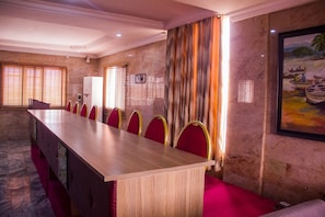 Un salón de conferencias con una larga mesa, sillas rojas y un cuadro en la pared.