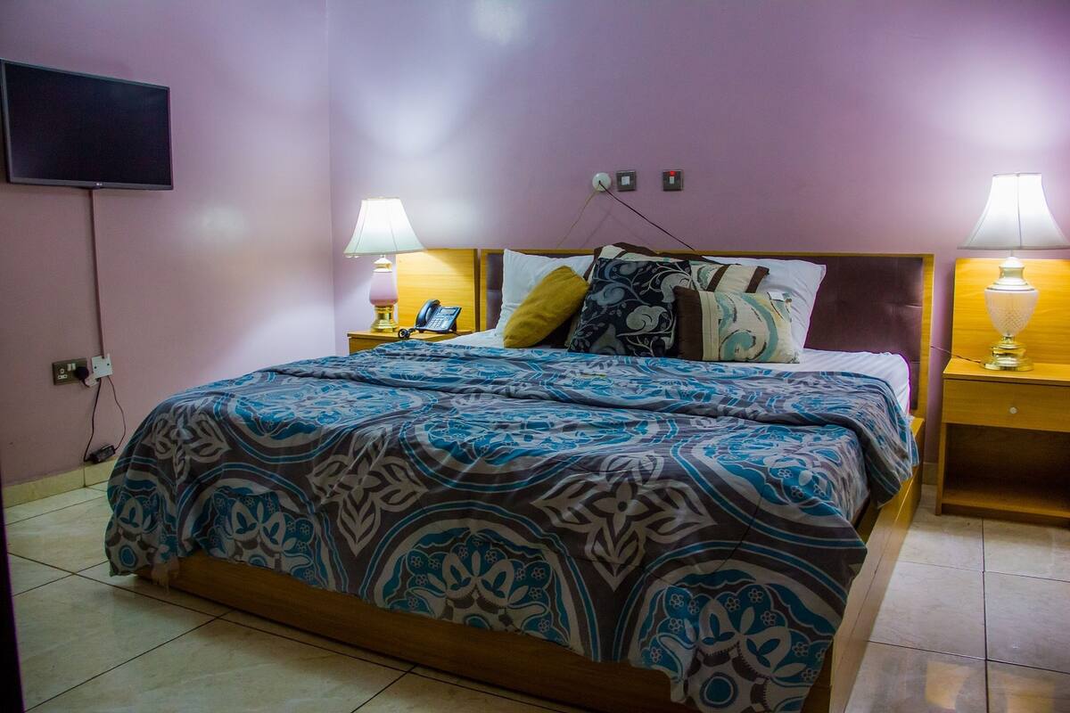 Un dormitorio con cama, dos lámparas de noche, un teléfono y televisión montada en la pared.